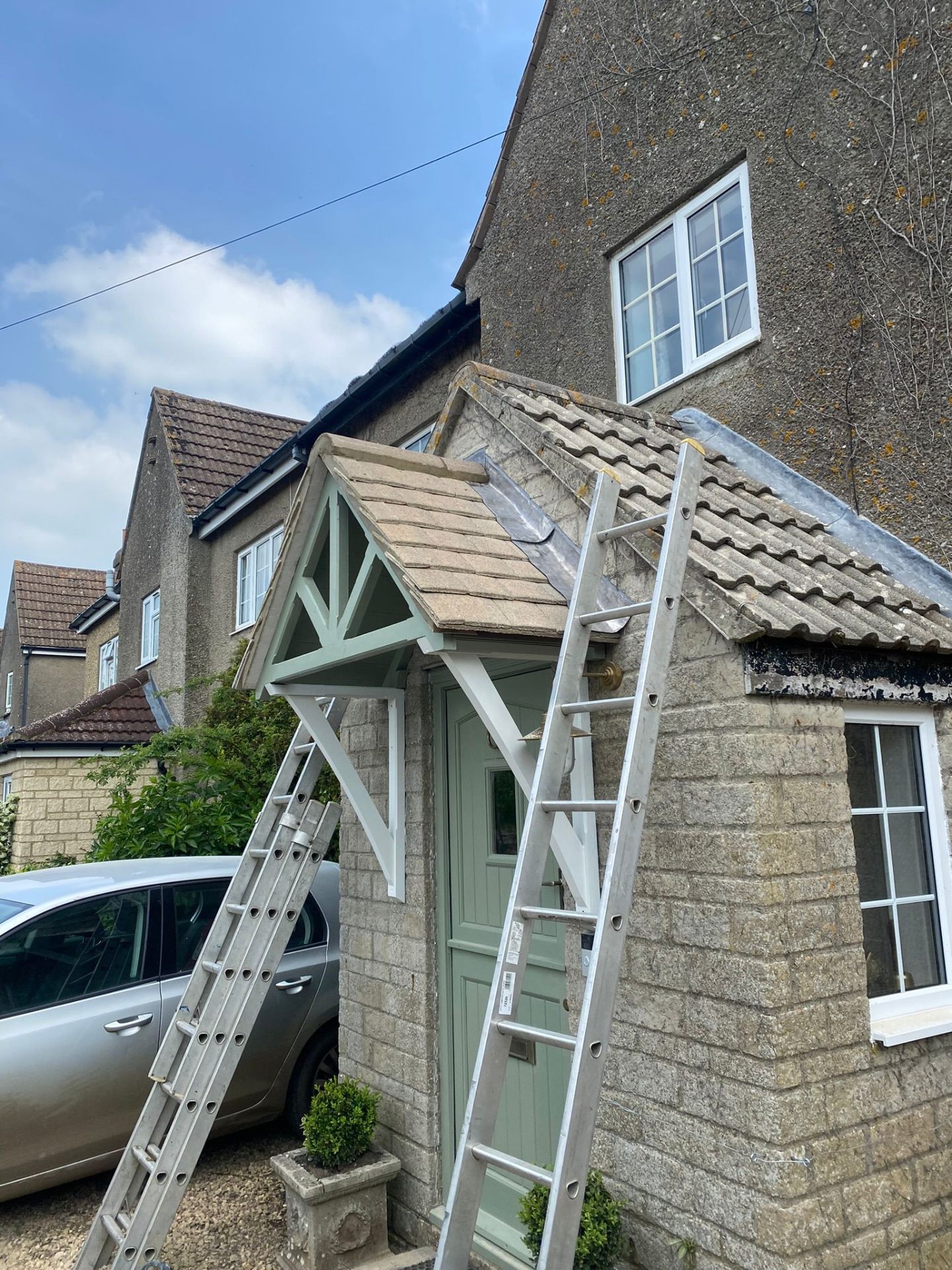 Traditional Cotswold stone cottage with ladders positioned for roof tile repairs