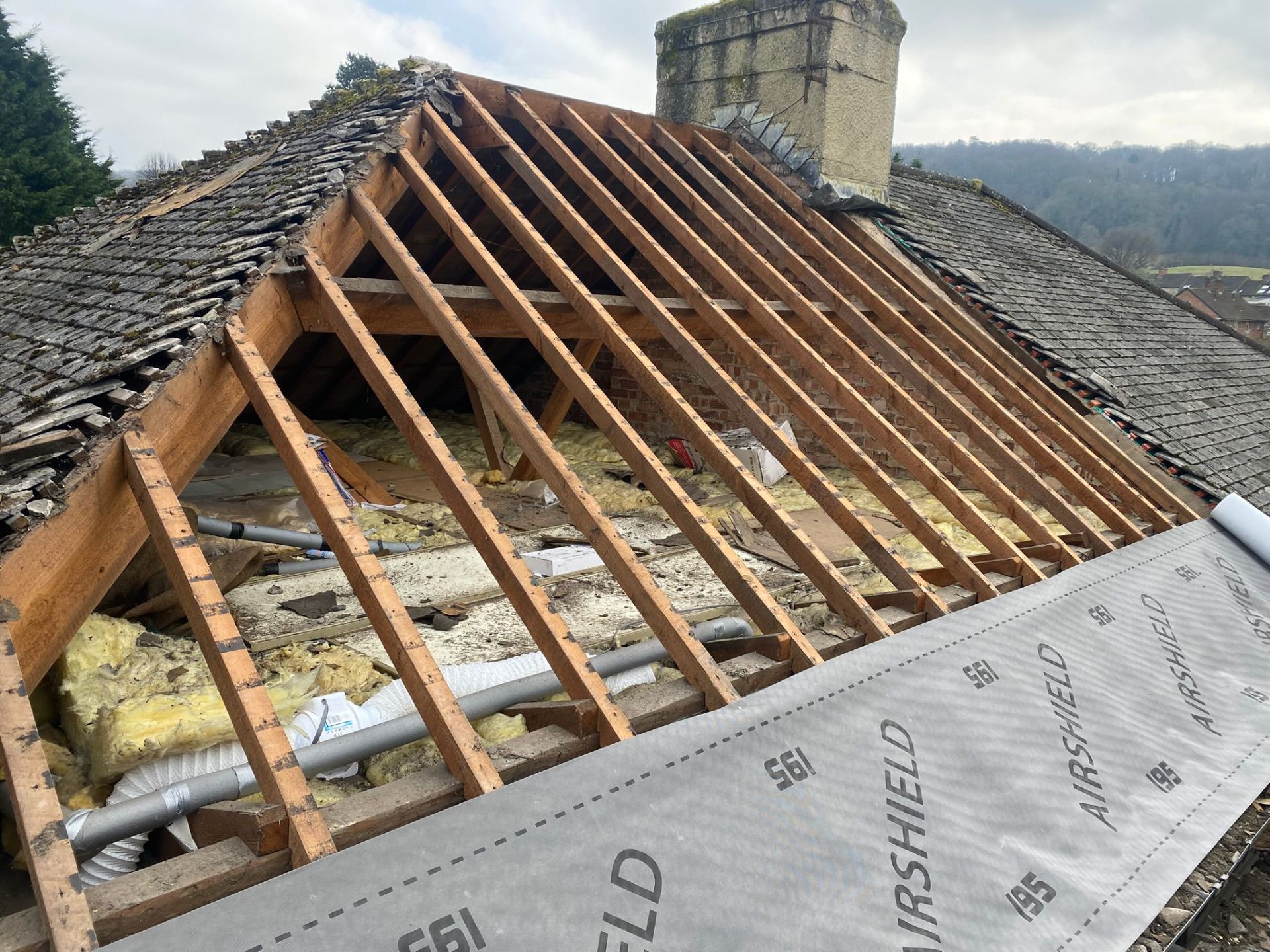Exposed roof structure during strip-down showing rafters and insulation before re-roofing